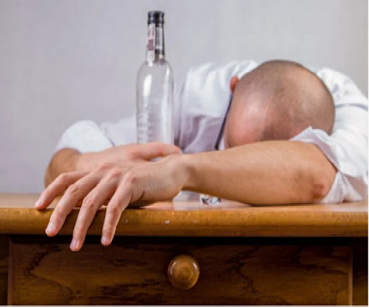 Man with head down on table next to empty alcohol bottle